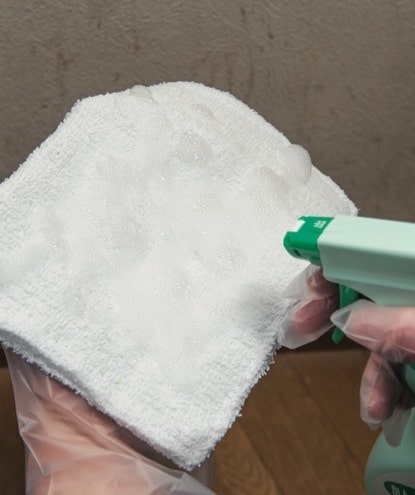 使い切りの手袋をはめ、雑巾に洗剤をスプレーする。まずは、壁全体を下拭きして軽く汚れを取る。
