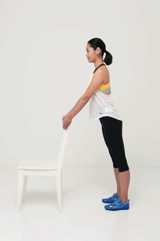 足を腰幅に開き、椅子の背を両手で掴んで立つ。体がやや前傾姿勢になるように。