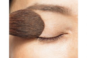 1. チークブラシに透明のフェイスパウダーを含ませ、まつ毛の際からまぶた全体、さらに眉毛まで覆うようにのせる。このひと手間で、パウダーが皮脂を吸着し、メイクの持ちがよくなる。