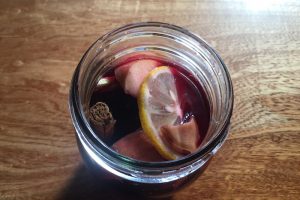 2. ガラス瓶に1のりんごとレモンシナモンスティック、生はちみつ漬けの生姜と生姜のハニーシロップを加えて赤ワインを注ぐ。（甘めの赤ワインを使う場合はフルーツからも甘みがでることを考慮して生姜のハニーシロップは入れなくとも良い）