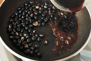 黒豆を再加熱して梅黒蜜を注ぎ、フライパンをゆすってからめる。