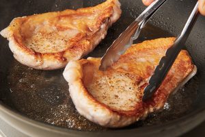 4.反り返っていたら、トングなどで押さえて均一に焼く。器に盛り、カリフラワーを添える。【POINT】肉は脂身が右側にくるように盛り付けるのが洋食の基本。