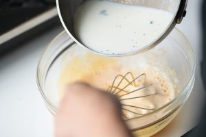 2.鍋に牛乳、バニラビーンズのさやとしごいた種を入れて沸騰直前まで温め、1のボウルに半量を入れてよく混ぜ、鍋に戻す。
