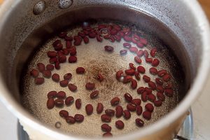 1. 豆(ささげ）は洗い、かぶるくらいの水を加えて強火にかけ、煮立ったらいったん茹で汁をこぼす。