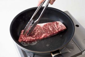 凍った肉は反ってくるため、トングで肉を押さえてフライパンに密着させるのが大事なポイント。