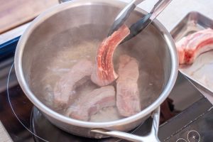 （1）ネギは白髪ネギにする。にんにくは潰す。しょうがは皮付きのままスライスする。鍋にたっぷりの湯を沸かし、スペアリブの表面の色が変わるまで中火でさっと茹で、ざるにあげる。