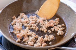 （2）フライパンにごま油を中火で熱し、鶏ひき肉を炒める。