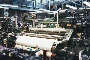 旧式のシャトル織機：経糸が大きく開いたところにシャトルという器具が入って緯糸を紡いで織り上げていく