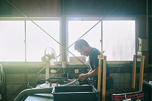 棕櫚を挟む作業を行う山本さん。手前にある筒は作業の工程で棕櫚の繊維から出る木屑を吸い込む集塵機