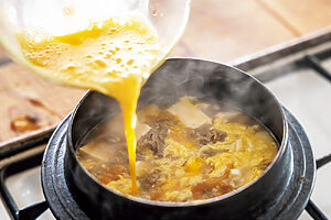 8. 木綿豆腐を入れてひと煮立ちさせ、溶き卵を加え、お玉で軽く混ぜる。器に盛り付け、長ねぎをのせて黒こしょうをふる。塩味は、食べながら好みでキムチや塩（共に分量外）を加えて調整する