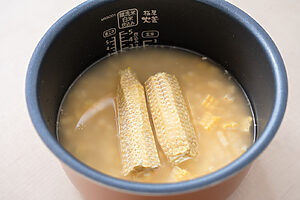 （2）炊飯器に米、酒、塩を入れ、2合の目盛りまで水を加える。とうもろこしの実と芯をのせて炊飯する
