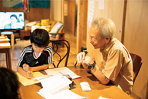 施設内では、利用者が自由気ままに過ごしている。元エンジニアの男性は、小学生に夏休みの宿題を教えている様子