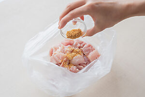 （2）鶏もも肉をポリ袋に入れ、酒、顆粒コンソメ、にんにく、塩、こしょうを加えてよくもみ込み、10分ほど置く