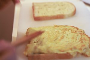 2. 卵焼き器に胡麻油を熱して卵液を投入したら、箸で手早くかき混ぜながらふんわりさせる。火が通りすぎないほうが断然おいしいので、焼くのは片面だけ。火は中強火。卵が焼けたら海苔の上にのせ、黒胡椒をふった食パンで挟む。