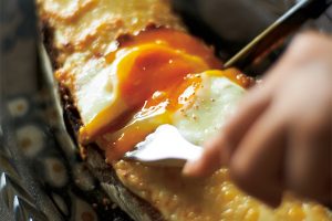 【熟成したチーズをのせ、 厚めのパンを堪能。クロックマダム 】作り置きしてあるベシャメルソースを生クリームでのばし、スープキューブ（ビオのもの）と塩で味をつける。厚めにスライスしたカンパーニュにベシャメルソースをのせ、白こしょうをふり、削ったグリュイエルチーズをたっぷりのせたら、予熱しておいたオーブンで焼く。その間にフライパンにバターをひき、ごくごく弱火で目玉焼きを作る。焼きあがったパンにのせて完成。